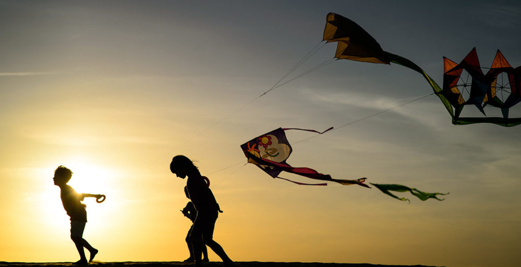 children flying single line kites against a sunset