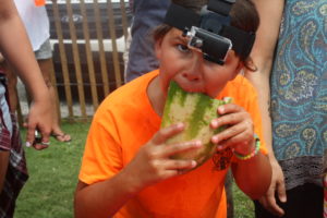A kid with a go pro strapped to his head takes a bite out of his watermelon