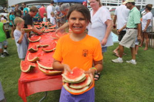 A girl smiles at the camera holding watermelon rind
