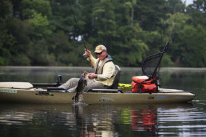 A fisherman holding up a fish he just caught while sitting in a Hobie Fishing Kayak