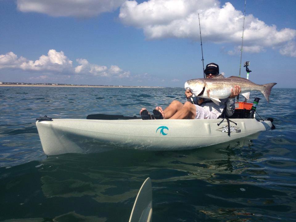 A fisherman holding up a big fish that he caught while sitting in a Hobie Fishing Kayak