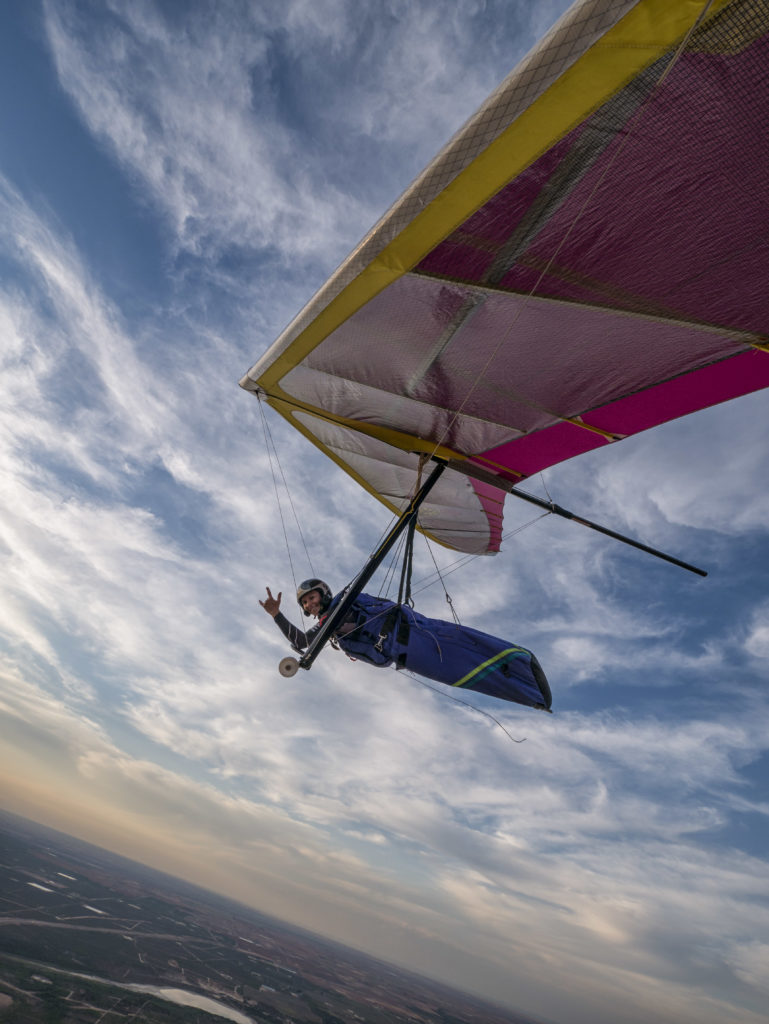 Sara Weaver flying high above the ground in a hang glider