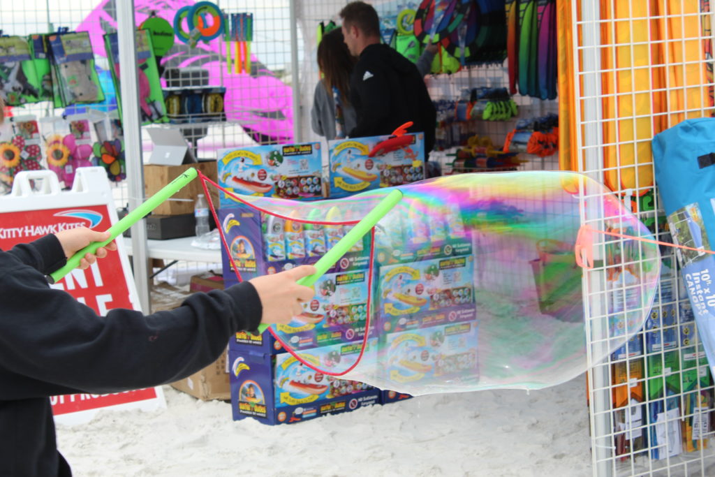 Bubble wand toy being played with in front of the Kitty Hawk Kites retail tent at the 2022 Fly into Spring Kite Festival